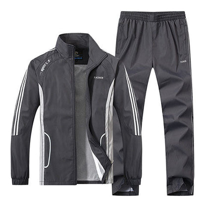 Grauer Trainingsanzug für Herren, bestehend aus Jacke und Hose, mit weißen Streifen und Reißverschluss. Sportbekleidung, atmungsaktiv, modisch.