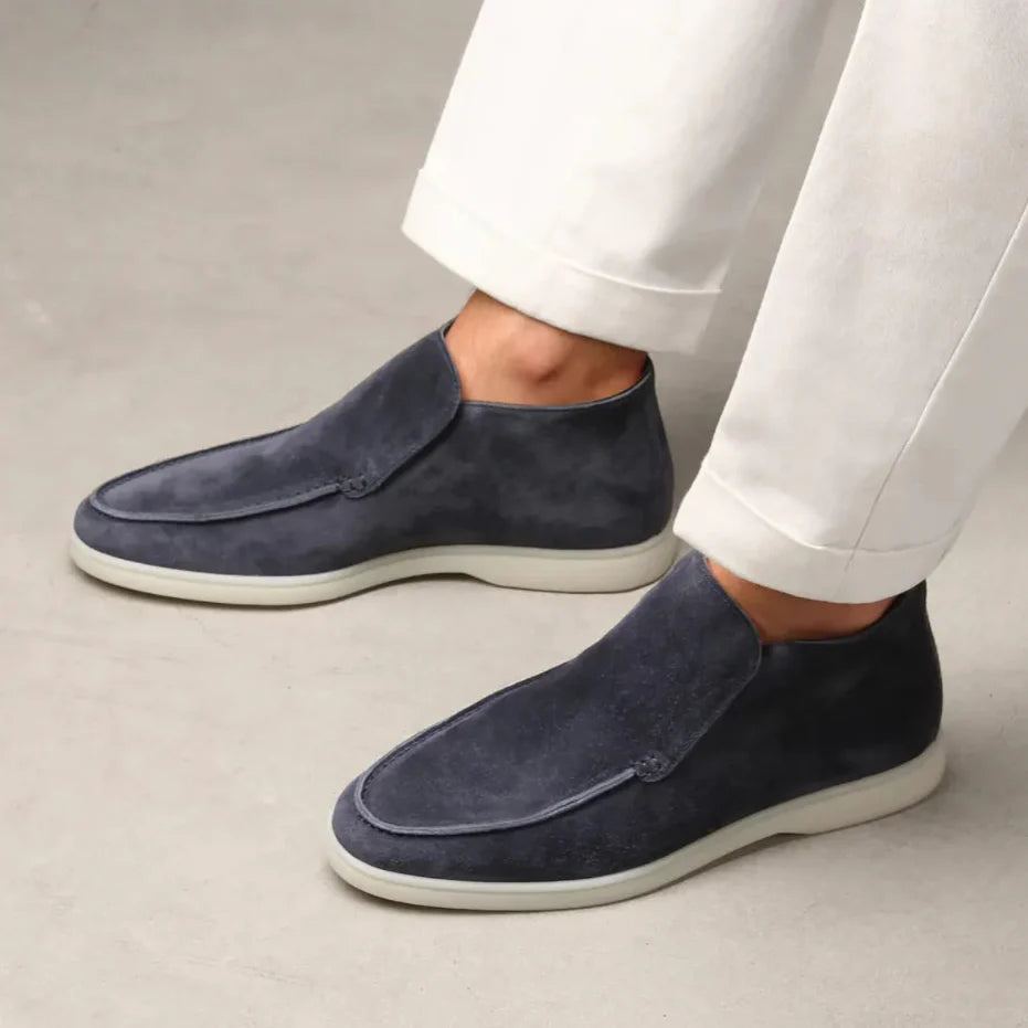 Dunkelblaue Herren-Slipper aus Wildleder, getragen mit weißen Hosen. Elegante, bequeme Schuhe für stilvolle Freizeit- und Business-Looks.