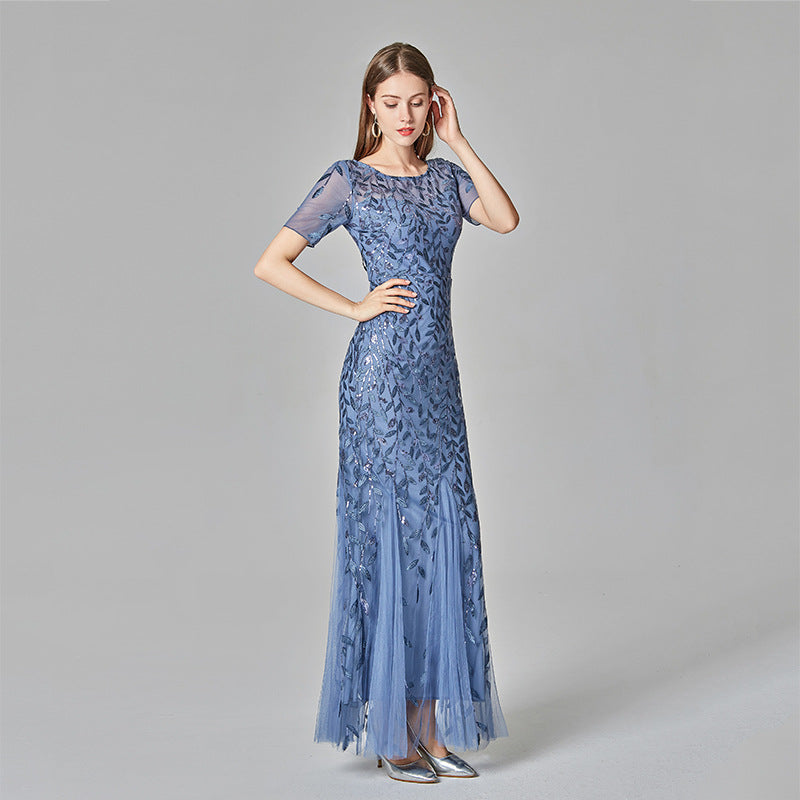 Frau in elegantem, blauem Abendkleid mit Pailletten und Tüll, stehend vor grauem Hintergrund. Perfekt für formelle Anlässe und Modeevents.