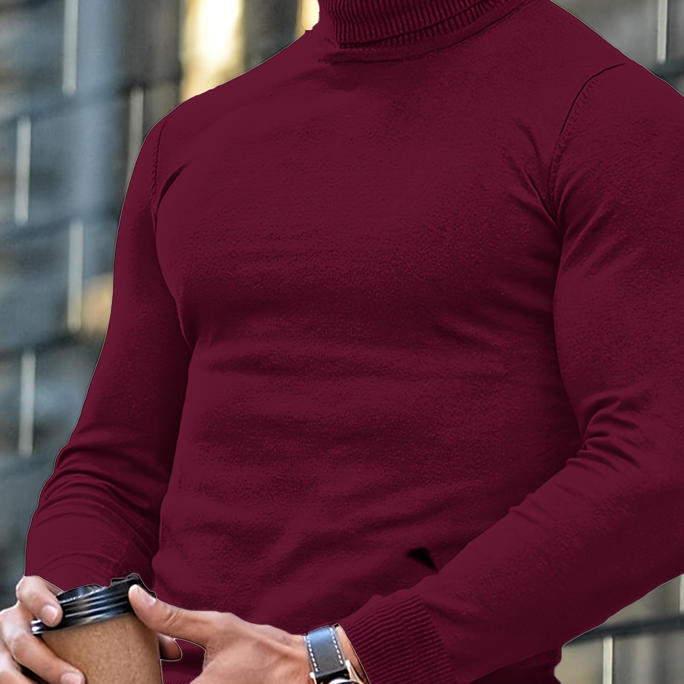 Mann in bordeauxrotem Rollkragenpullover hält Kaffeebecher, trägt Armbanduhr. Urbaner Hintergrund, modischer Herbstlook, stilvolle Herrenmode.