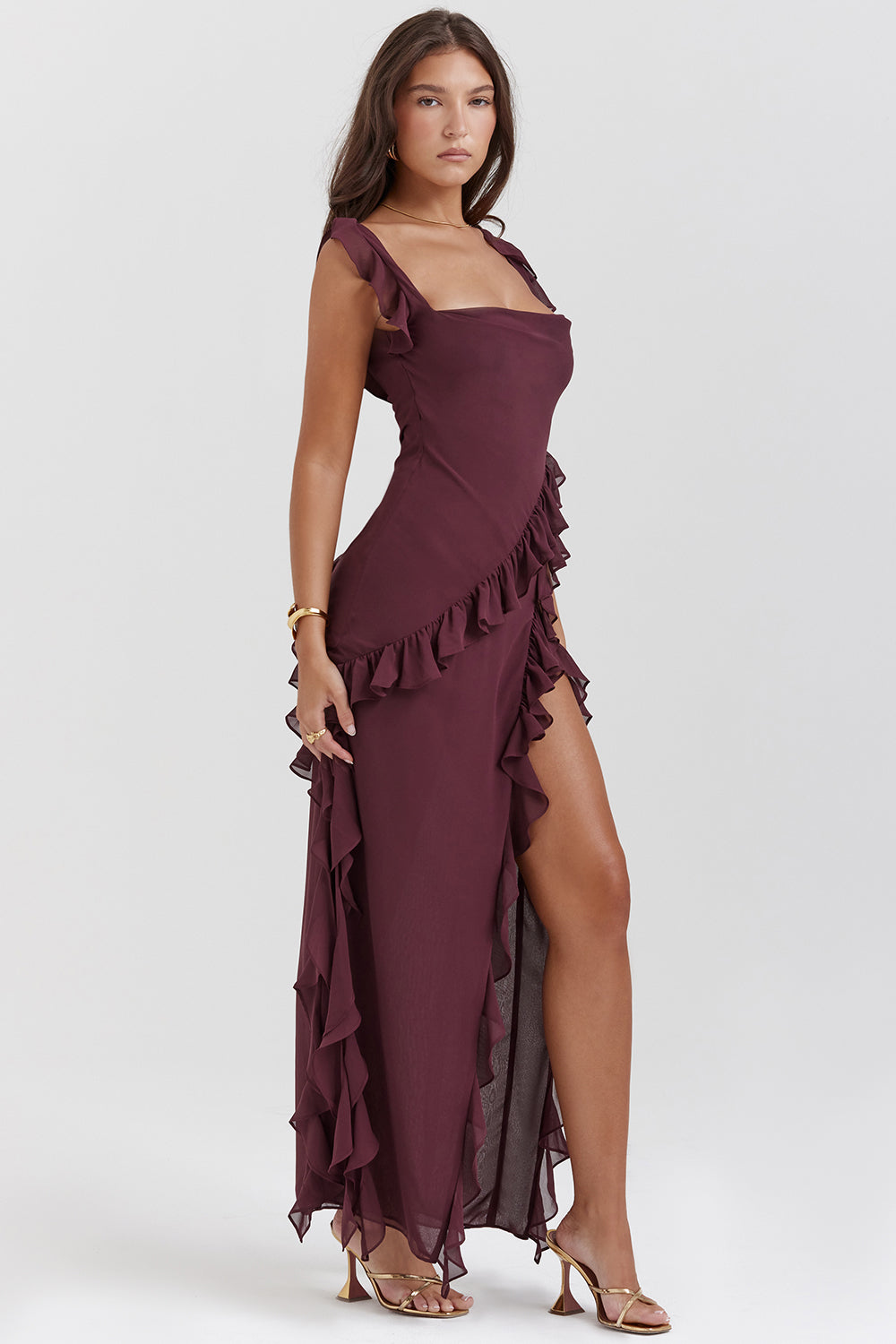 Frau in elegantem, weinrotem Abendkleid mit Rüschen und hohem Beinschlitz, goldene Sandalen, modisches Outfit, stilvolle Abendmode.