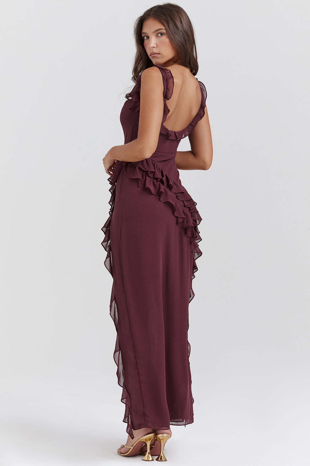 Frau in elegantem, rückenfreiem, weinrotem Abendkleid mit Rüschen, stehend, seitlich, auf weißem Hintergrund. Perfekt für formelle Anlässe.