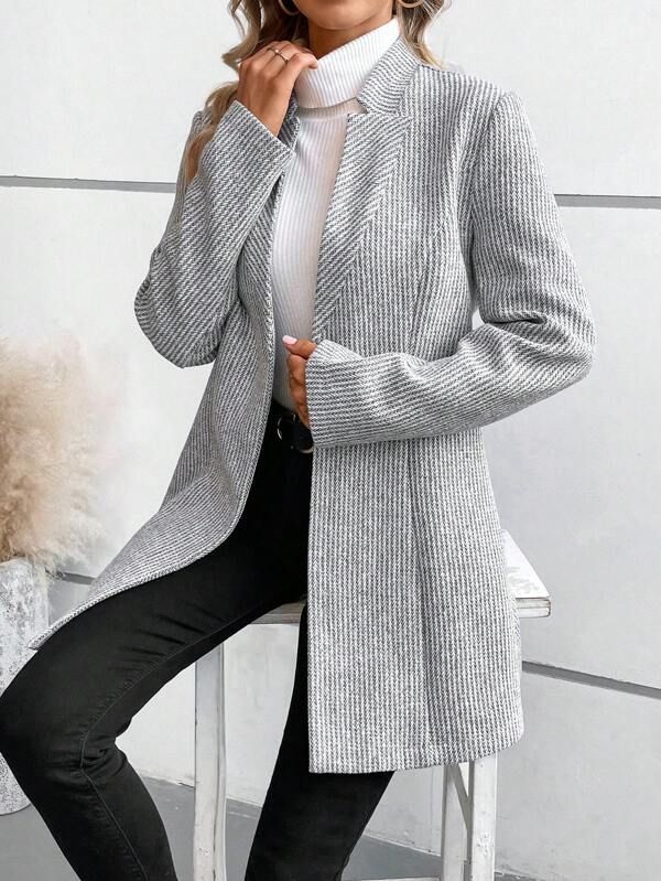 Frau in grauem gestreiftem Blazer und weißem Rollkragenpullover, sitzt auf einem Stuhl. Modetrend, elegante Damenbekleidung, Herbstmode.