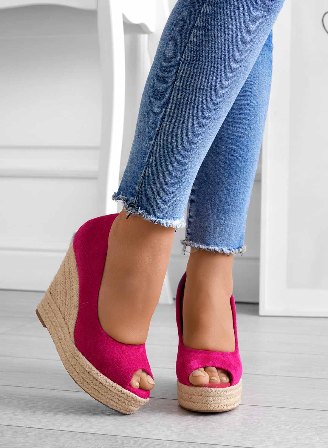 Frau trägt pinke Keilabsatz-Sandalen mit offener Spitze und blauen Jeans. Modische Sommerschuhe, Damenmode, trendige Keilabsätze.
