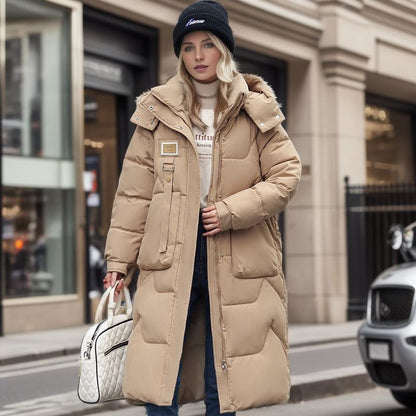 Blonde Frau in beigem Daunenmantel und schwarzer Mütze, hält weiße Handtasche, steht auf städtischer Straße vor einem Geschäft. Wintermode, Streetstyle.