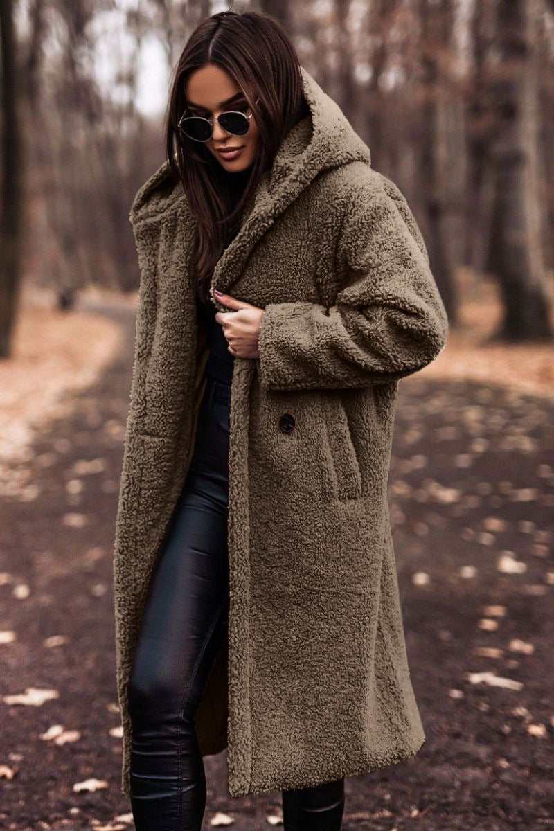 Frau im braunen Teddy-Mantel und Sonnenbrille spaziert im herbstlichen Wald. Modetrend, Herbstmode, stilvoller Look, Outdoor-Bekleidung.