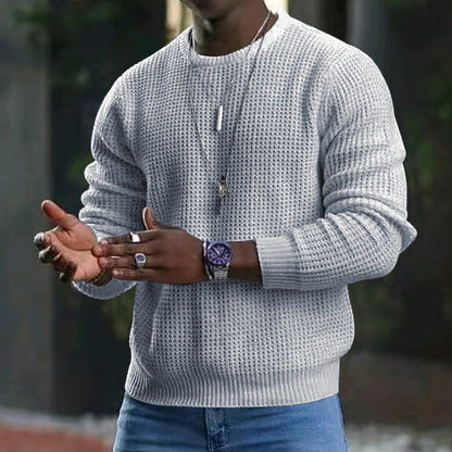 Mann in grauem Strickpullover, trägt Armbanduhr und Halskette, gestikuliert mit Händen. Mode, Herrenbekleidung, Accessoires, urbaner Stil.