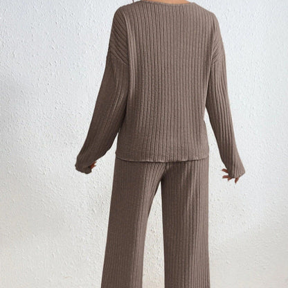 Braunes, geripptes Strick-Set für Damen, bestehend aus langärmligem Pullover und weiter Hose, vor weißer Wand. Bequemes, modisches Loungewear-Outfit.