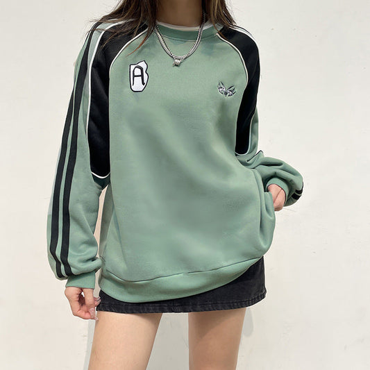 Grünes Sweatshirt mit schwarzen Streifen und Logo, getragen von Person. Modischer Pullover, lässiger Stil, ideal für Herbstmode und Streetwear.