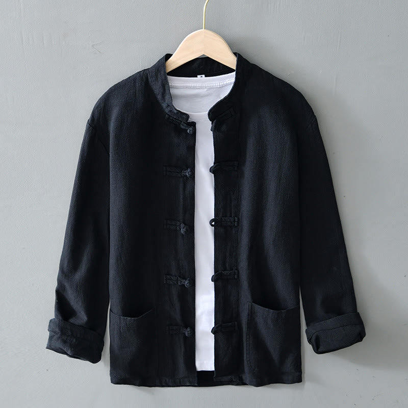 Schwarze, traditionelle chinesische Jacke mit Stehkragen und Knotenverschlüssen, hängt auf einem Kleiderbügel vor grauem Hintergrund.