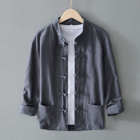Graue Herrenjacke im chinesischen Stil mit Stehkragen und Knöpfen, über weißem T-Shirt, auf Holzkleiderbügel vor grauer Wand.