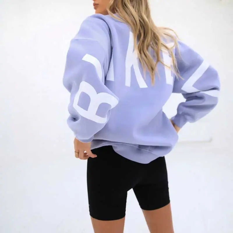 Frau in lila Oversize-Sweatshirt mit weißem Aufdruck und schwarzen Radlerhosen, Rückansicht. Modetrend, lässiger Stil, Streetwear.