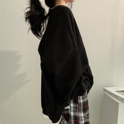 Frau in schwarzem Oversize-Pullover und karierten Hosen, seitlich stehend, vor weißer Wand. Modetrend, lässiger Stil, Herbstmode.