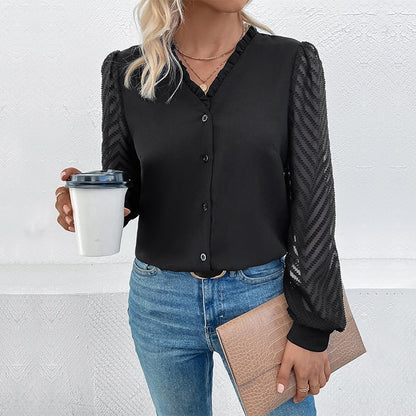 Frau in schwarzer Bluse mit transparenten Ärmeln, hält Kaffeebecher und beige Clutch, trägt blaue Jeans. Elegante Freizeitmode, Damenoutfit.