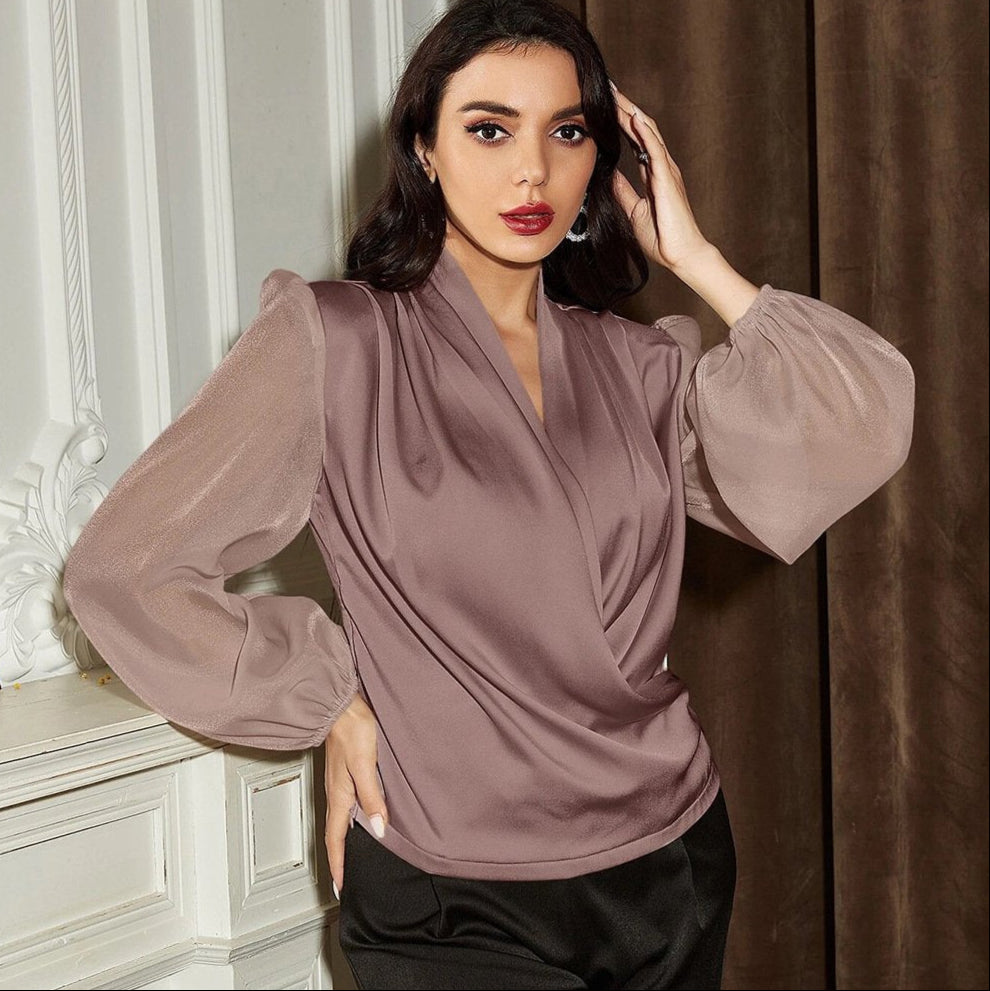 Frau in eleganter, langärmeliger, lila Bluse mit V-Ausschnitt, posiert vor weißer Wand. Modetrend, Damenmode, stilvolle Kleidung.