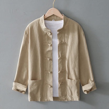 Beige Herrenjacke aus Leinen mit Stehkragen, Knopfleiste und aufgesetzten Taschen, über weißem T-Shirt auf Holzkleiderbügel vor grauer Wand.