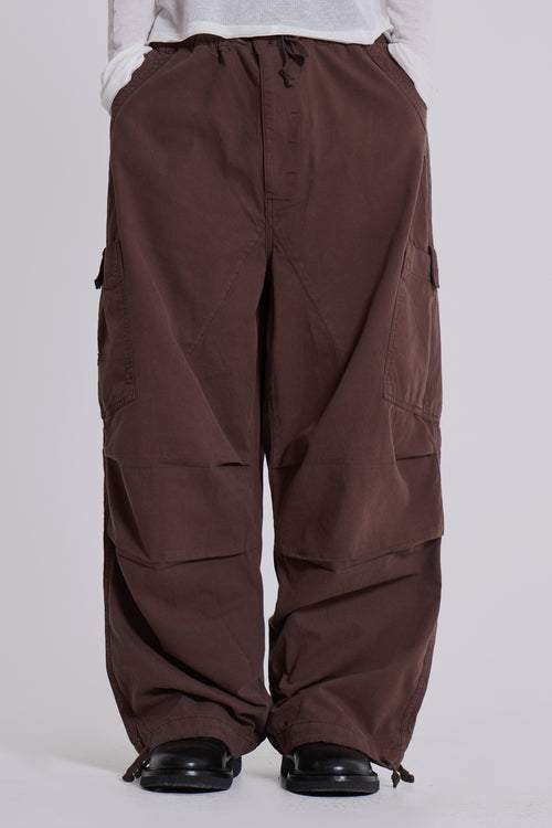 Braune Baggy-Hose mit großen Seitentaschen, lässiger Stil, getragen von Person in weißem Oberteil, modische Streetwear, bequeme Passform.