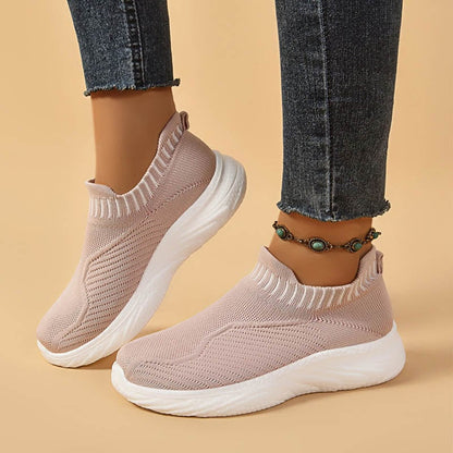 Damen Sneaker in Rosa, gestricktes Design, weiße Sohle, kombiniert mit blauen Jeans und einem modischen Fußkettchen auf beigem Hintergrund.