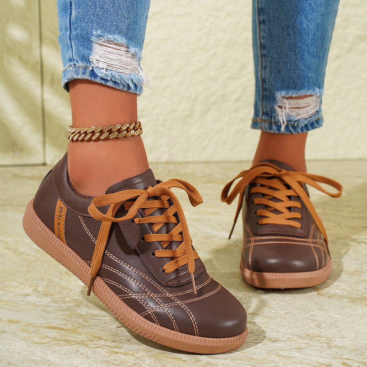 Damen Sneaker braun mit hellbraunen Schnürsenkeln, kombiniert mit zerrissenen Jeans und goldfarbenem Fußkettchen. Modische Freizeitschuhe.