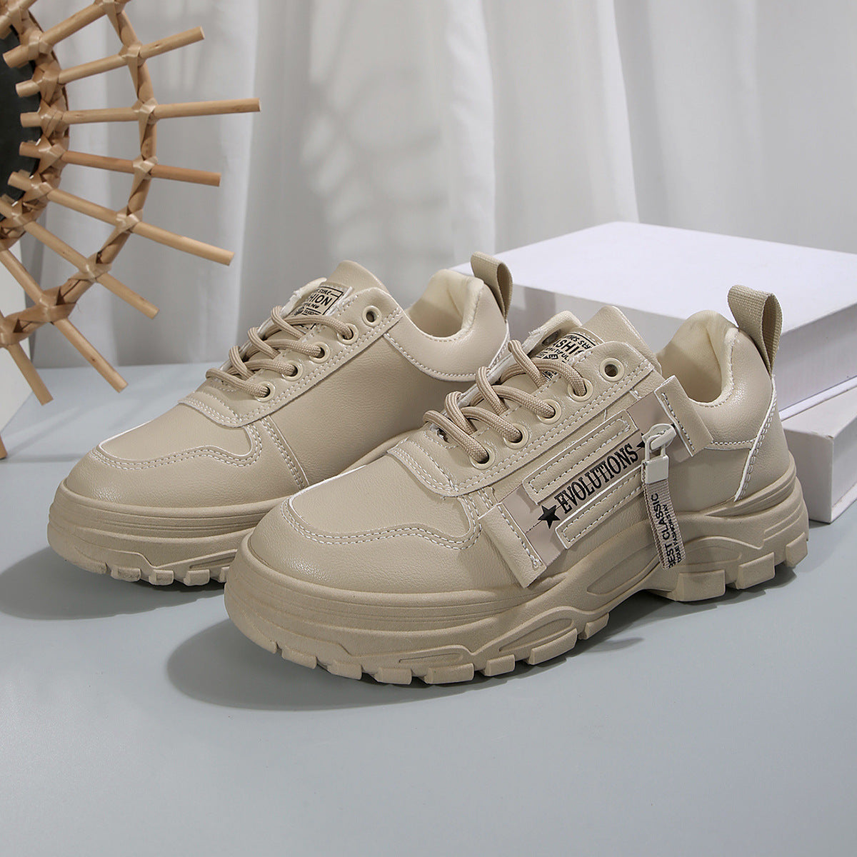 Beige Sneaker mit dicker Sohle und seitlichem Reißverschluss, modisches Design, ideal für Streetwear und Freizeit, auf grauem Hintergrund.
