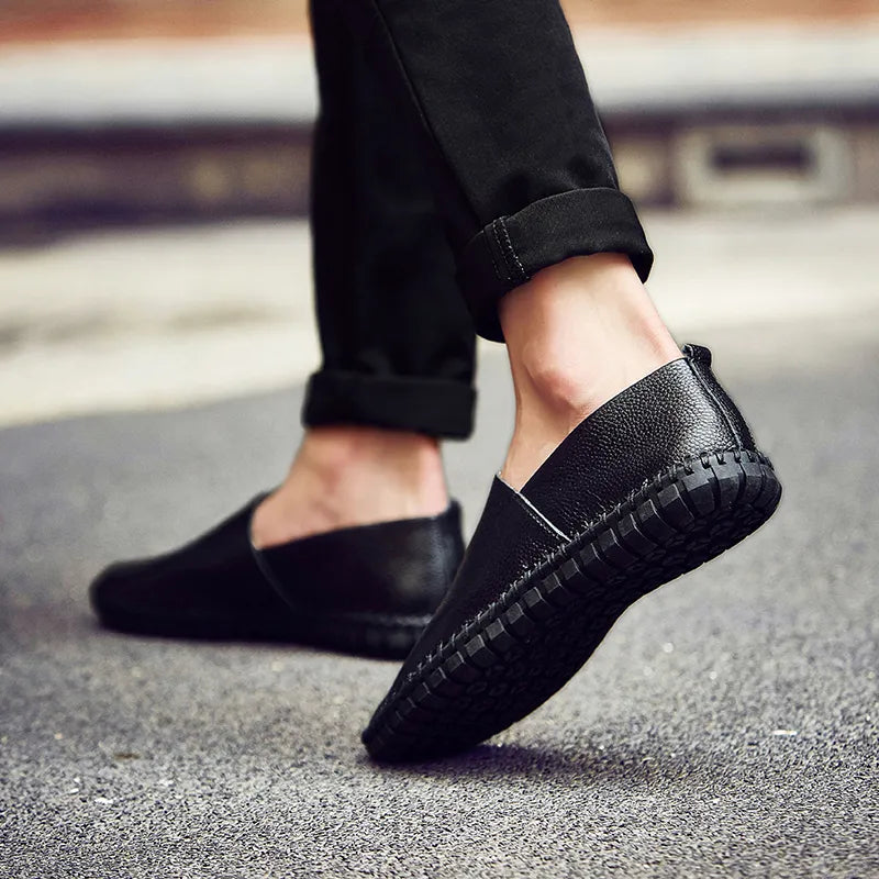 Schwarze Herren-Slipper aus Leder auf Asphalt, lässiger Stil, bequeme Passform, ideal für Freizeitkleidung und modische Outfits.