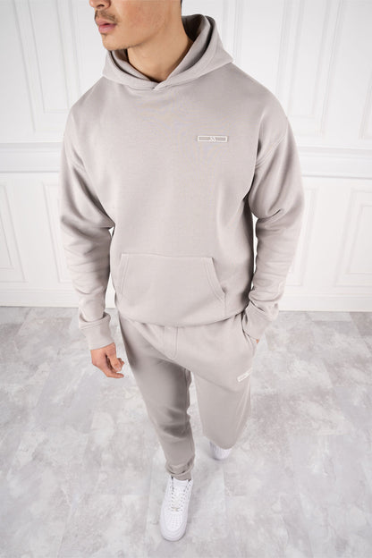 Mann in grauem Hoodie und Jogginghose, steht auf hellem Marmorboden, weiße Sneakers, moderne Freizeitmode, stilvoller Look.