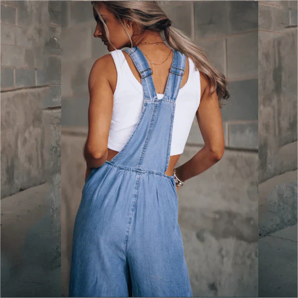 Frau in blauer Jeans-Latzhose und weißem Top, Rückansicht. Modetrend, lässiger Stil, urbaner Hintergrund. Perfekt für Sommermode und Streetwear.