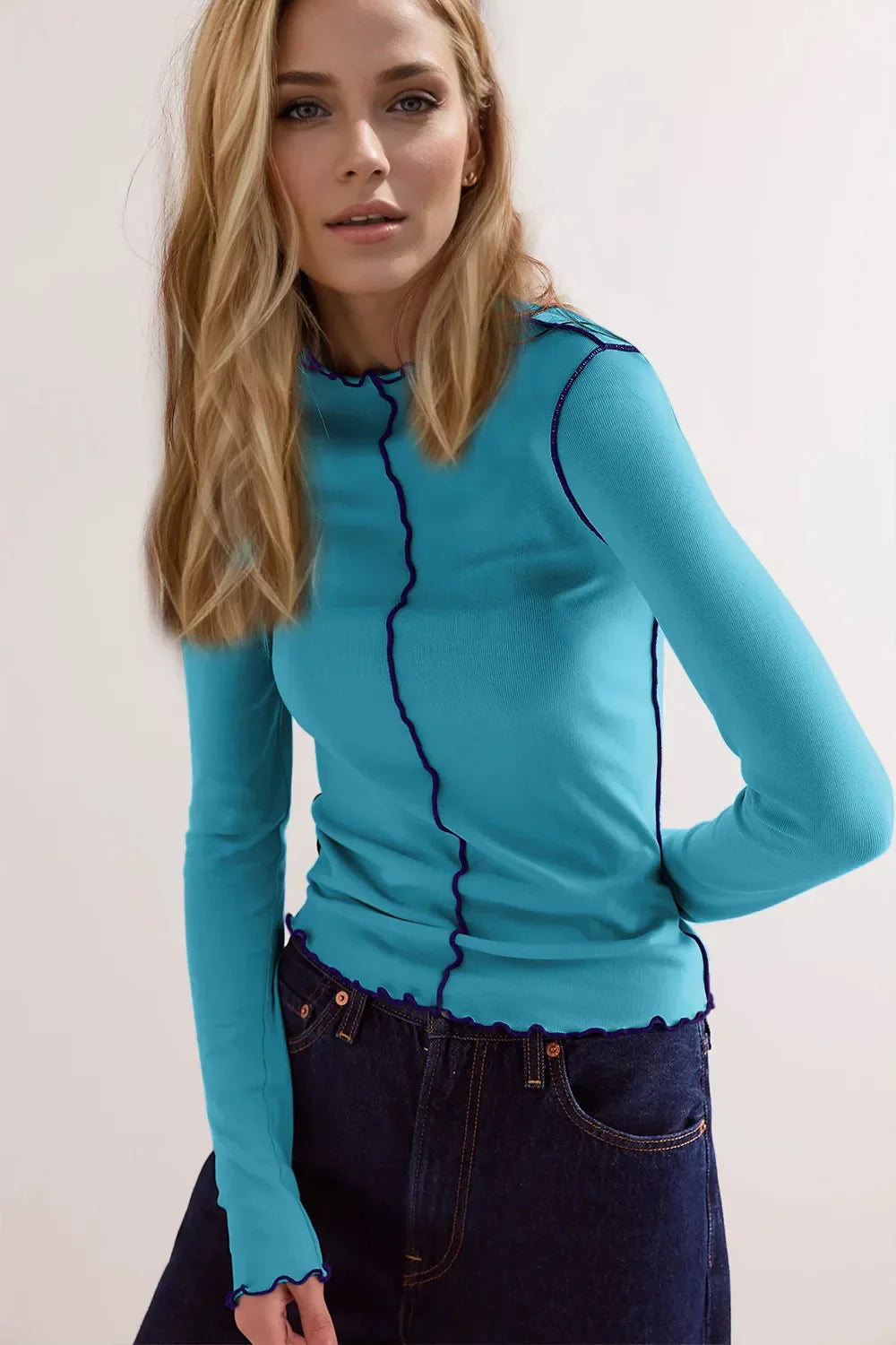 Blonde Frau in blauem Langarmshirt mit welligen Nähten und blauer Jeans. Modetrend, Damenbekleidung, Freizeitlook, stilvolle Kleidung.