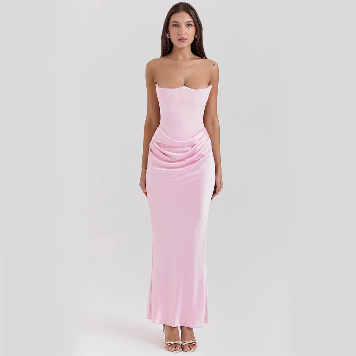 Frau in elegantem, schulterfreiem, rosa Abendkleid mit Raffung, stehend vor neutralem Hintergrund. Perfekt für formelle Anlässe und Modeevents.