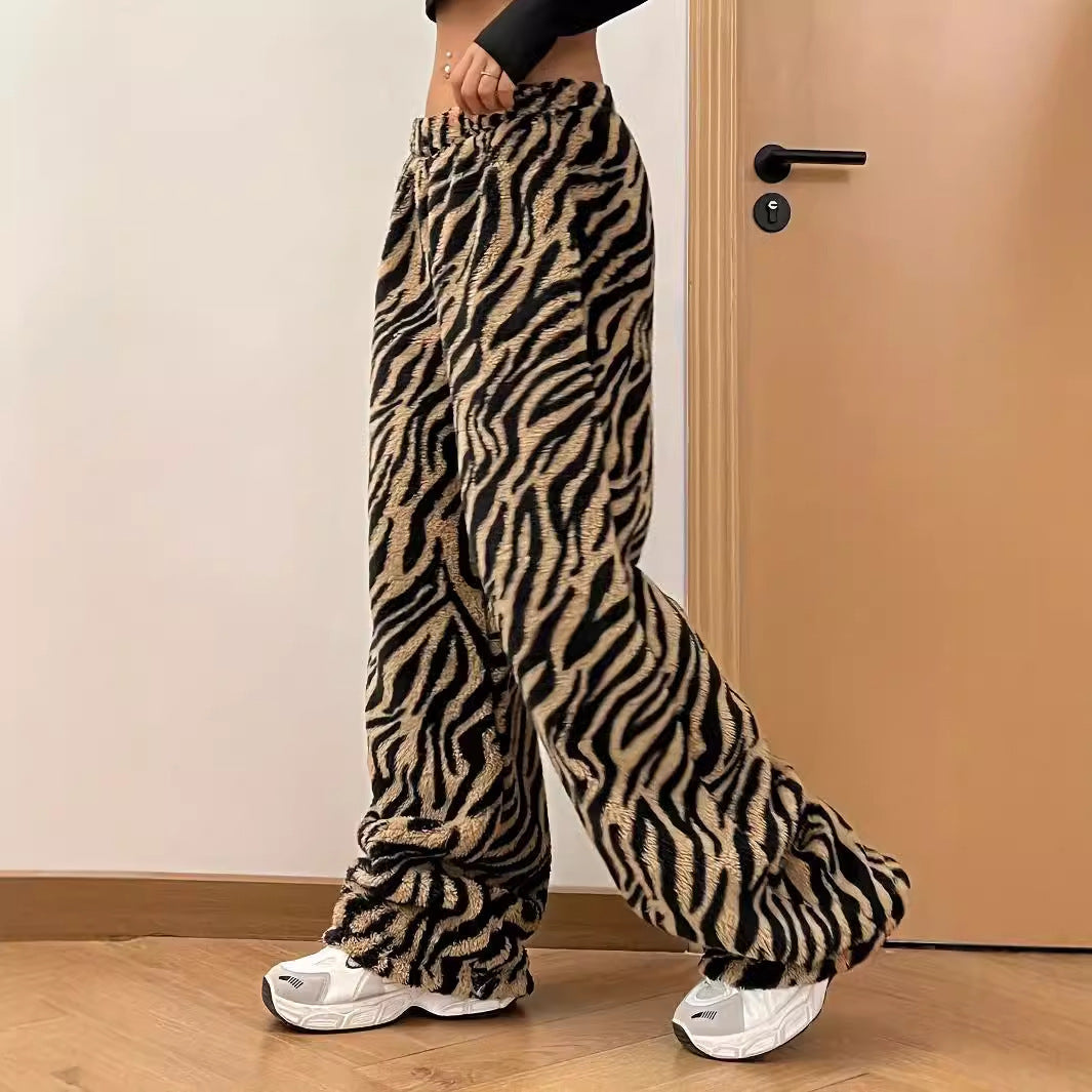 Frau trägt weite Hose mit Zebramuster und weiße Sneaker, steht vor Holztür. Modetrend, Streetwear, Animal-Print, bequeme Kleidung.