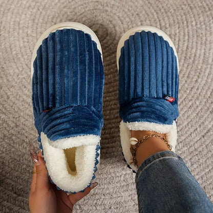 Blaue, gestreifte Hausschuhe aus Plüsch mit weißem Innenfutter auf einem grauen Teppich. Bequem, warm, ideal für den Winter.