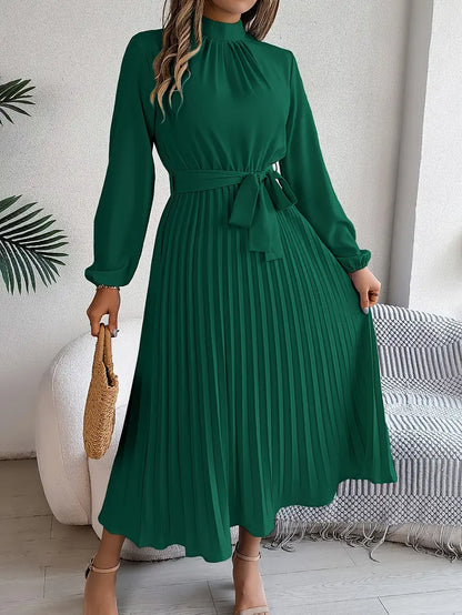 Frau in elegantem, langem, grünem Plisseekleid mit Gürtel, hält eine Strohtasche. Perfekt für Frühling, Sommermode, stilvoller Look.