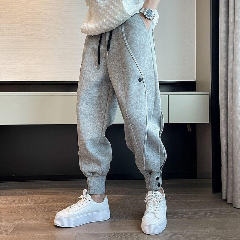 Graue Jogginghose mit schwarzen Kordeln und Knöpfen, kombiniert mit weißen Sneakers. Moderne Freizeitmode für Herren, ideal für sportlichen Look.