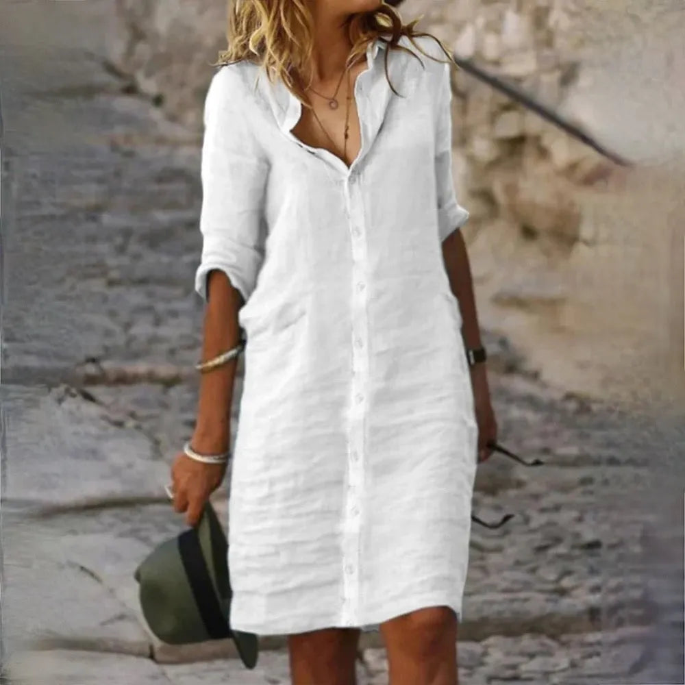 Frau in weißem Leinenkleid auf Kopfsteinpflaster, Sommermode, lässiger Stil, elegantes Design, modische Damenbekleidung, Outdoor-Szene.