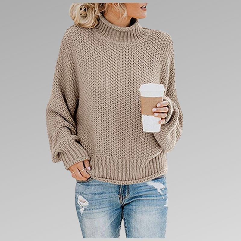 Frau in beigem Strickpullover mit Rollkragen hält Kaffeebecher, trägt zerrissene Jeans. Modetrend Herbst, lässiger Look, gemütlicher Stil.