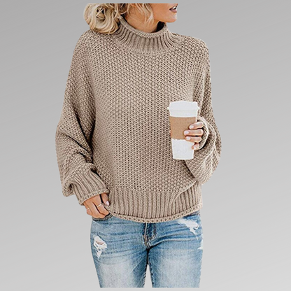 Frau in beigem Strickpullover mit Rollkragen hält Kaffeebecher, trägt zerrissene Jeans. Modetrend Herbst, lässiger Look, gemütlicher Stil.