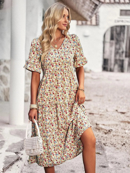 Blonde Frau in geblümtem Sommerkleid, hält weiße Handtasche, steht auf gepflasterter Straße. Modetrend, Sommermode, Damenkleid, Freizeitlook.