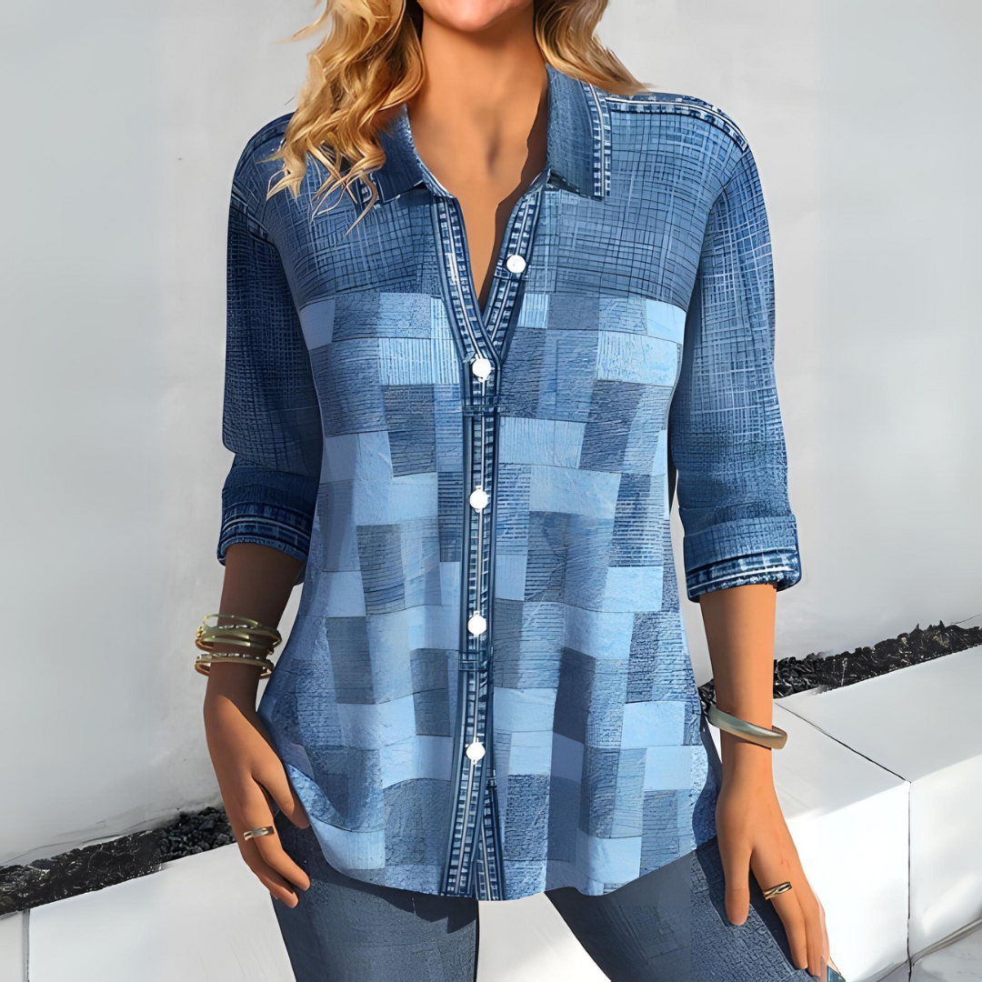 Frau in modischer, blauer Patchwork-Bluse mit Knöpfen, lässig gekleidet, trägt Armbänder, steht vor weißem Hintergrund. Trendige Damenmode.