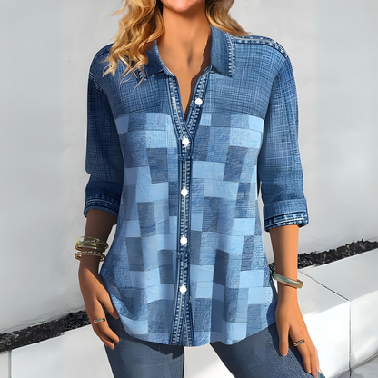 Frau in modischer, blauer Patchwork-Bluse mit Knöpfen, lässig gekleidet, trägt Armbänder, steht vor weißem Hintergrund. Trendige Damenmode.
