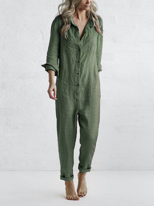 Frau in grünem Leinen-Jumpsuit, barfuß, vor weißer Wand. Modetrend, lässiger Einteiler, nachhaltige Kleidung, minimalistischer Stil.