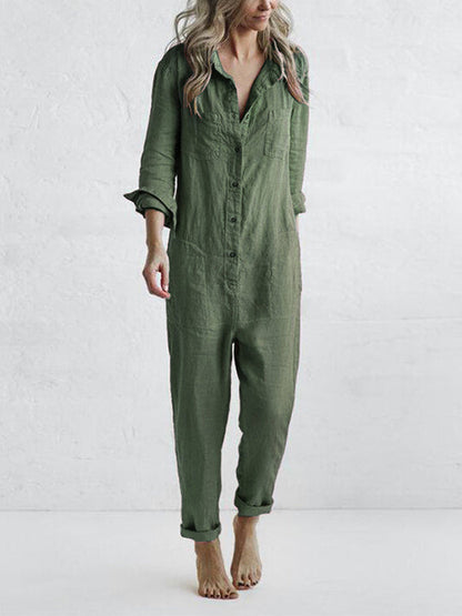 Frau in grünem Leinen-Jumpsuit, barfuß, vor weißer Wand. Modetrend, lässiger Einteiler, nachhaltige Kleidung, minimalistischer Stil.