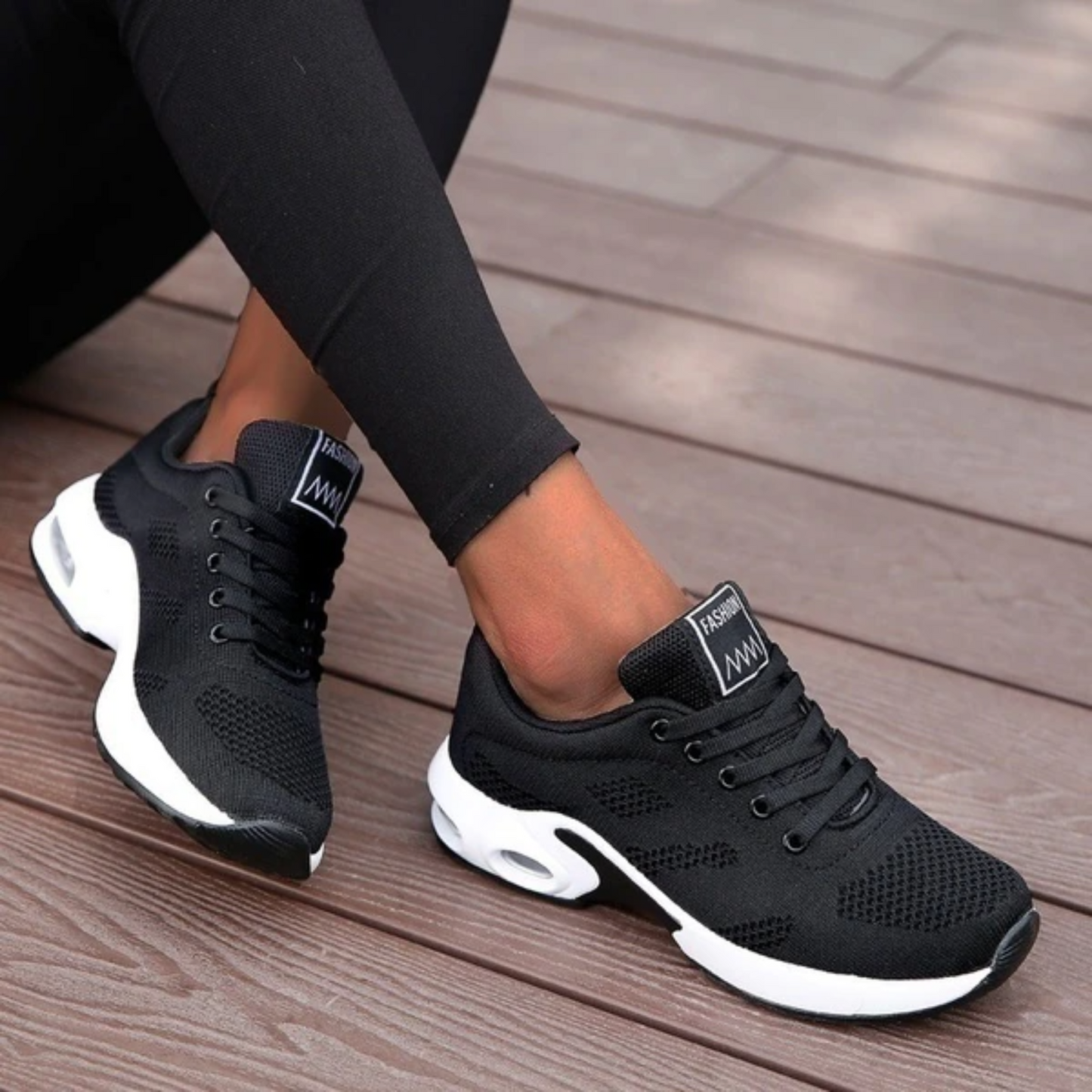 Schwarze Damen-Sneaker mit weißer Sohle auf Holzterrasse, modisch und bequem, ideal für Freizeit und Sport. Perfekte Passform und atmungsaktives Material.