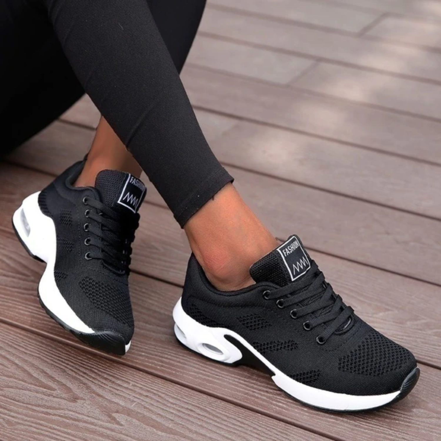 Schwarze Damen-Sneaker mit weißer Sohle auf Holzterrasse, modisch und bequem, ideal für Freizeit und Sport. Perfekte Passform und atmungsaktives Material.