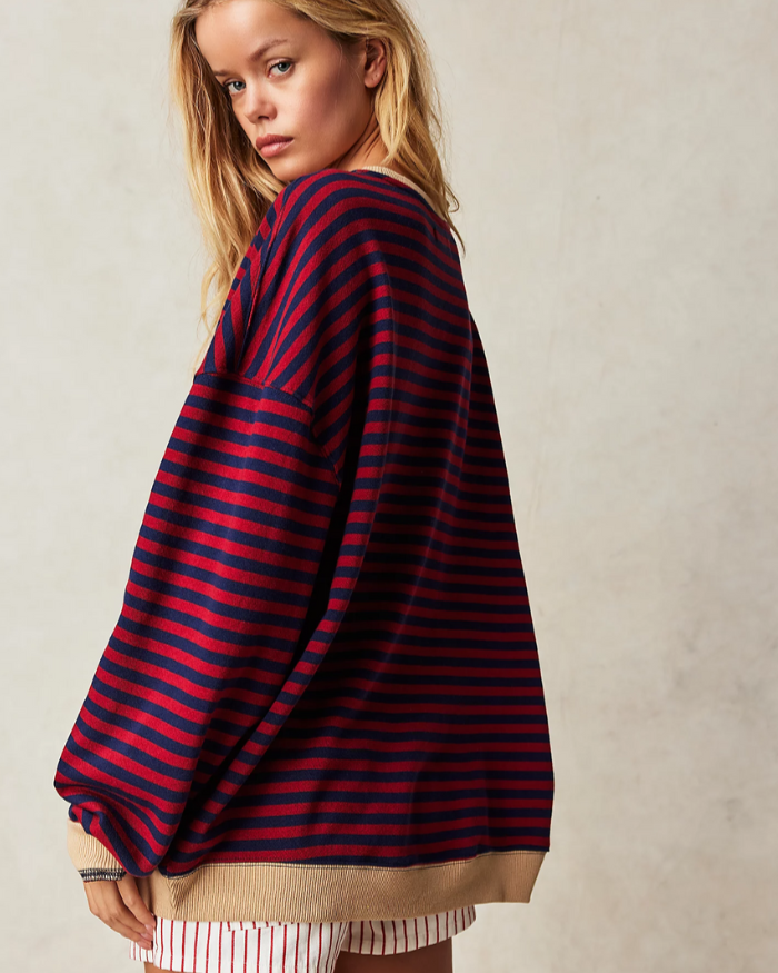 Blonde Frau in übergroßem, rot-blau gestreiftem Pullover, seitlich stehend. Modetrend, lässiger Stil, bequeme Kleidung, Herbstmode.