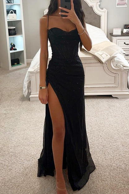 Frau in elegantem, schwarzem Abendkleid mit hohem Beinschlitz, steht in modernem Schlafzimmer. Perfekt für Gala, Ball oder Abendveranstaltung.