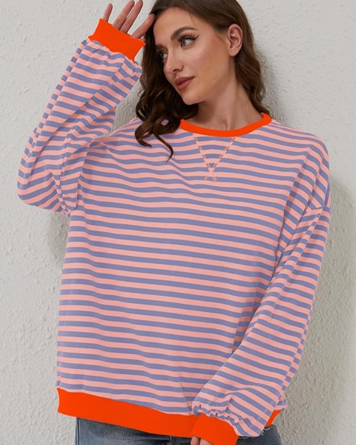 Frau trägt gestreiften Pullover in Rosa und Blau mit orangefarbenen Bündchen. Modetrend, lässiger Stil, Damenmode, bequeme Kleidung.