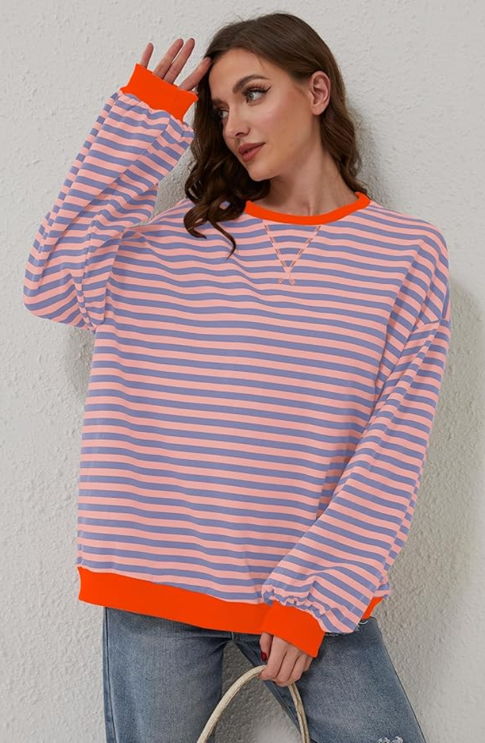 Frau in gestreiftem Pullover mit orangefarbenen Akzenten, lässig an Wand lehnend. Modetrend, Freizeitkleidung, Damenmode, gestreiftes Design.