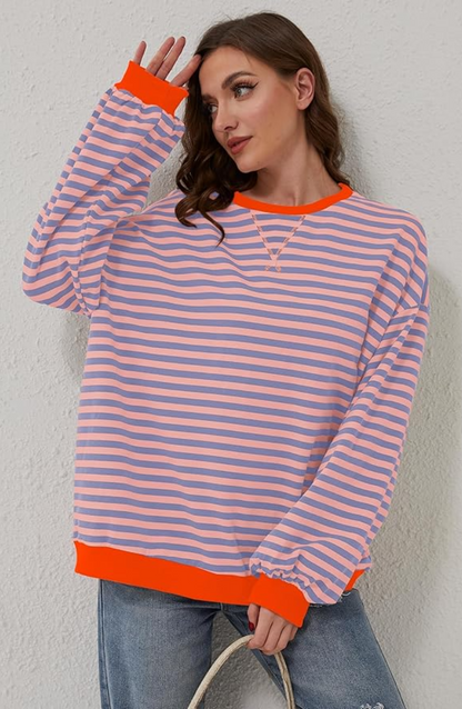 Frau in gestreiftem Pullover mit orangefarbenen Akzenten, lässig an Wand lehnend. Modetrend, Freizeitkleidung, Damenmode, gestreiftes Design.