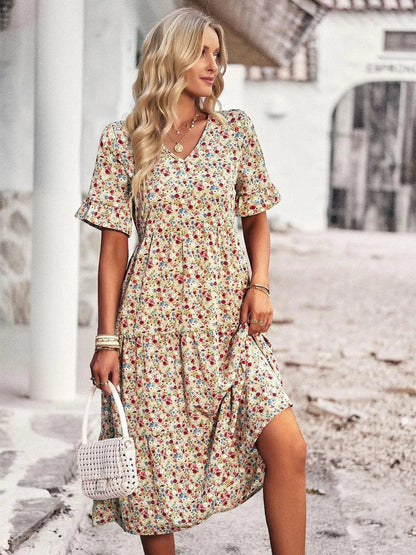 Blonde Frau in geblümtem Sommerkleid, hält weiße Handtasche, steht auf gepflasterter Straße. Modetrend, Sommermode, Damenkleid, Freizeitlook.