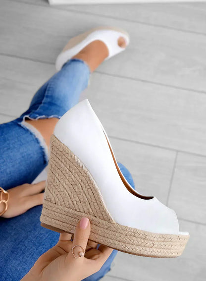 Frau hält weiße Keilsandalette mit Bastsohle, trägt zerrissene Jeans. Modische Sommerschuhe, Damenmode, bequeme Wedges.